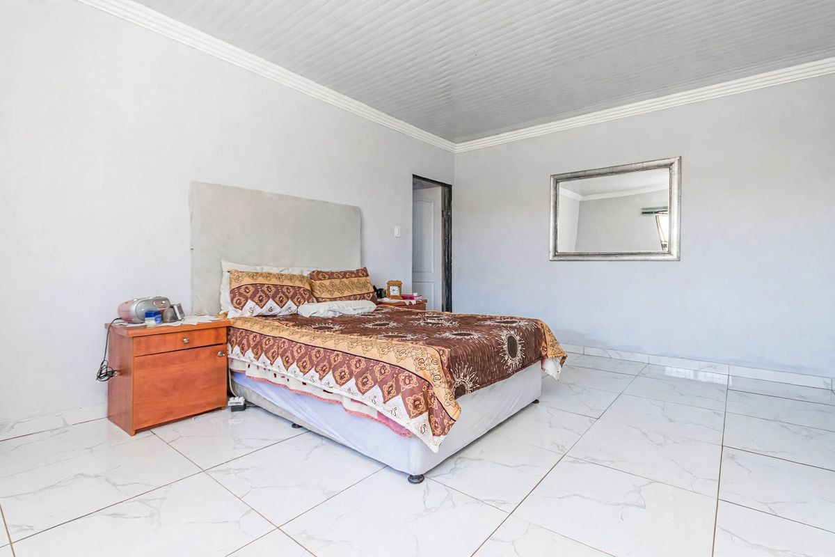 A spacious bedroom featuring large format white floor tiles and a panelled ceiling with decorative coving.