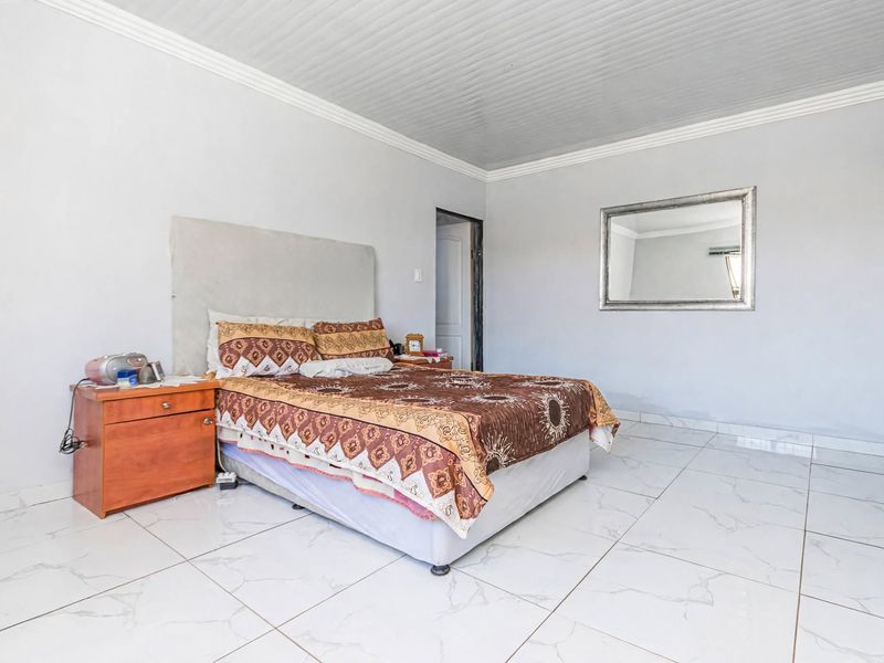 A spacious bedroom featuring large format white floor tiles and a panelled ceiling with decorative coving.