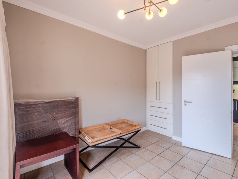 A clean, neutral bedroom featuring tiled flooring, a built-in wardrobe with drawers, and modern ceiling lighting.