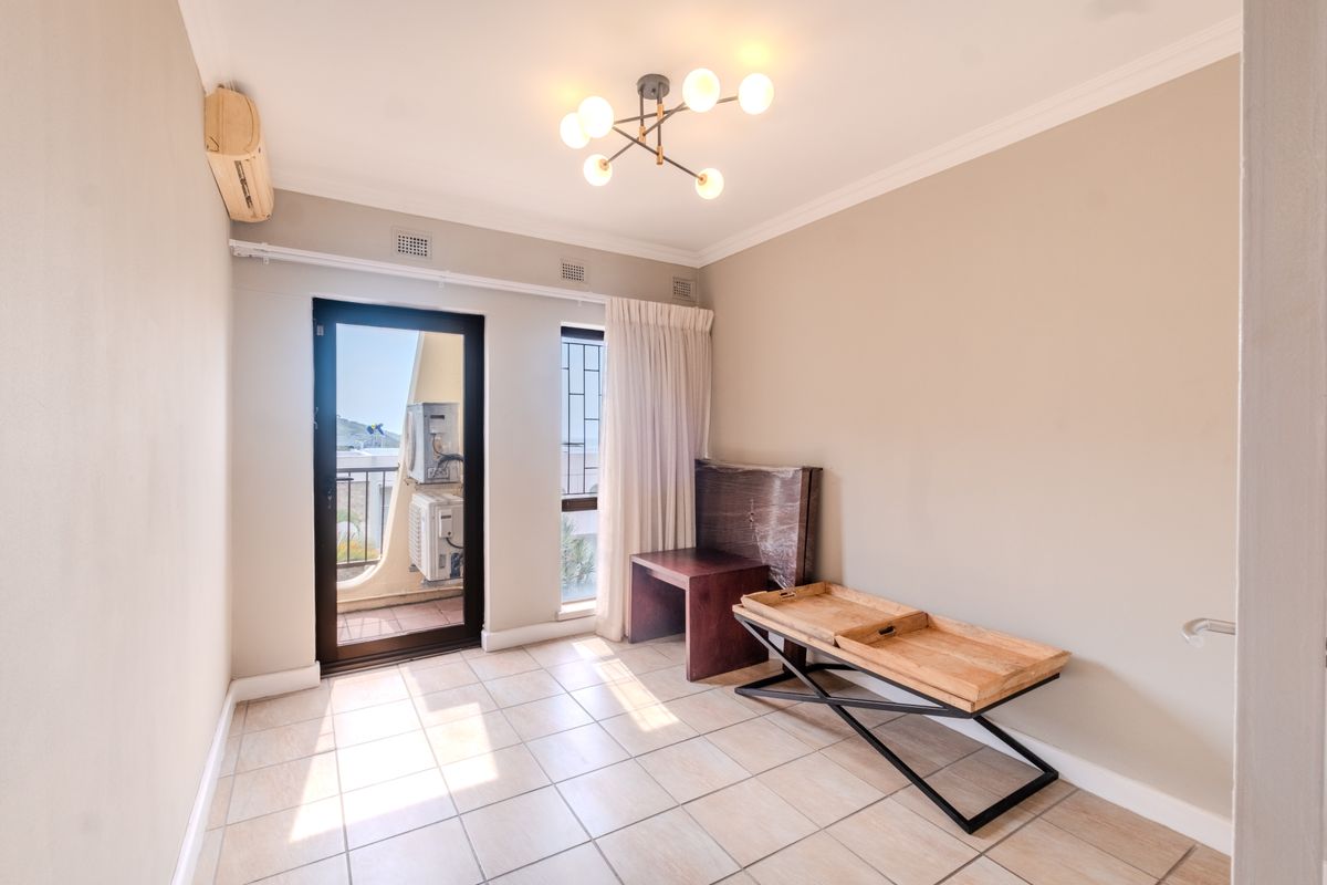 A bright, empty bedroom featuring tiled flooring, a modern ceiling light, and direct access to a private balcony through a glass door.