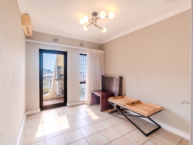 A bright, empty bedroom featuring tiled flooring, a modern ceiling light, and direct access to a private balcony through a glass door.