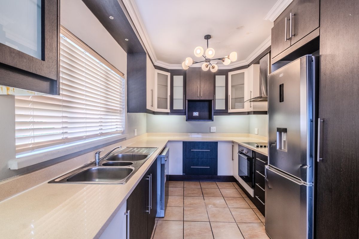 Modern kitchen featuring dark and light cabinetry, stone countertops, double basin sink, and integrated appliances with tiled flooring and ample natural light.