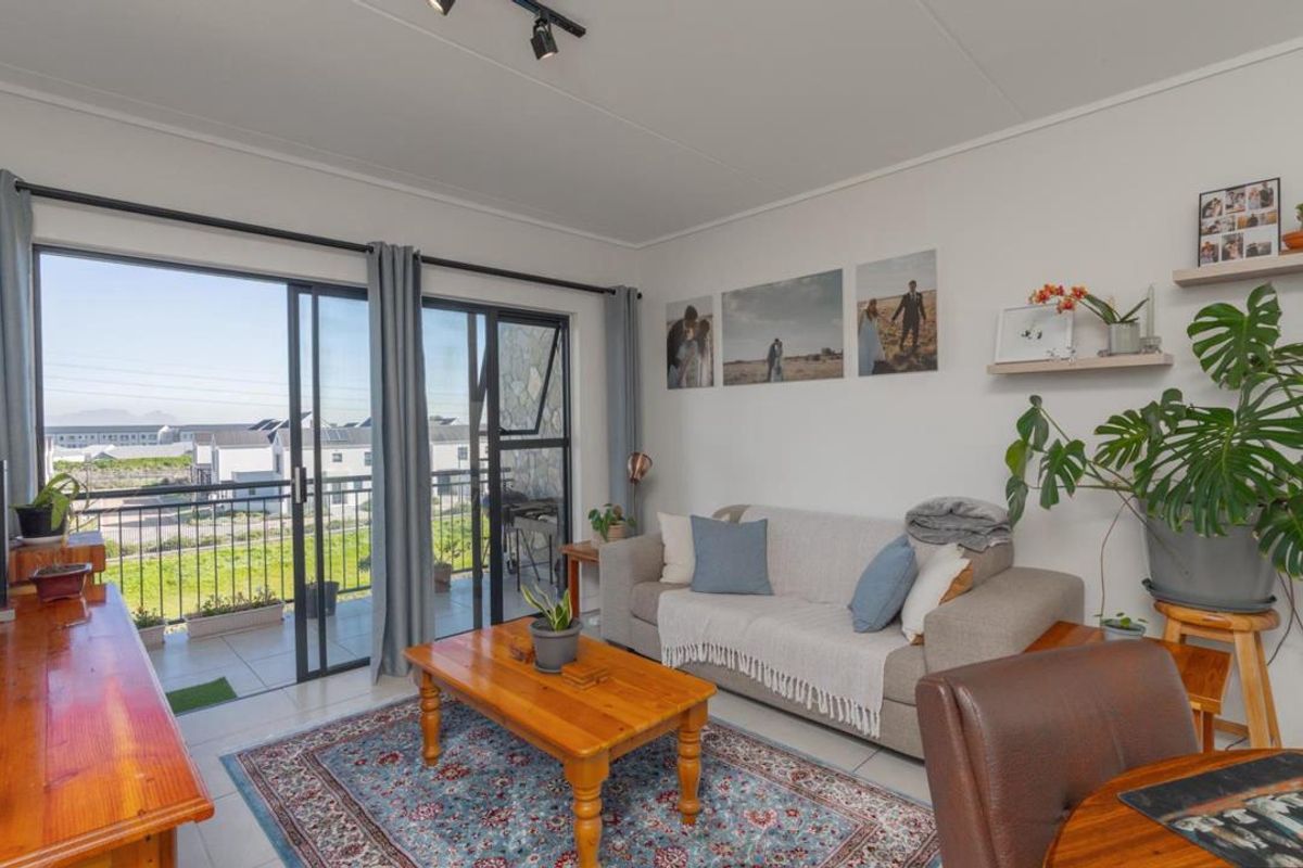 A bright living room featuring tiled flooring, track lighting, and large sliding glass doors that provide access to an outdoor balcony area.