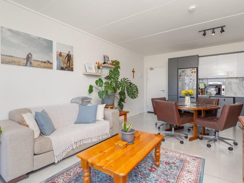 An open-plan living and dining area featuring modern grey and white kitchen cabinetry, marble-look splashback, and neutral tiled flooring throughout.