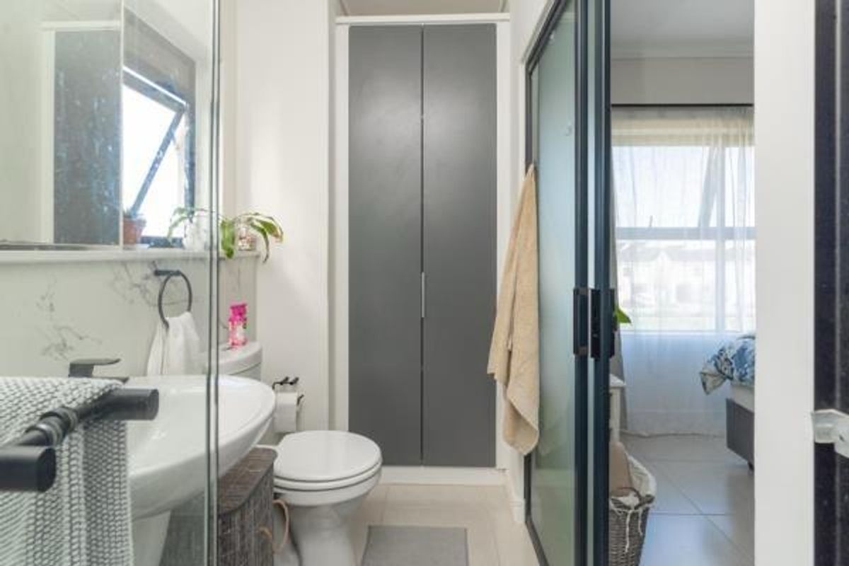 A modern bathroom featuring a pedestal basin, toilet, and a built-in storage cupboard, with a glass-enclosed shower and neutral tiled finishes.