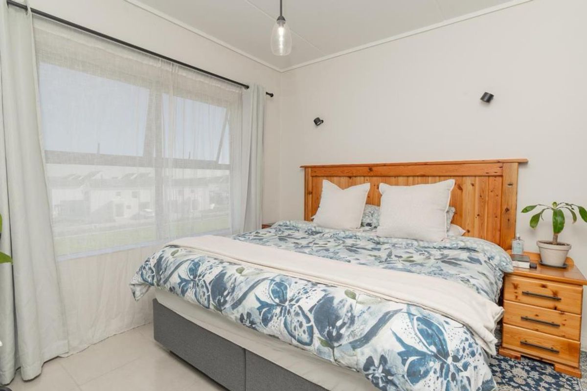A bright and well-maintained bedroom featuring a large window with natural light, neutral wall finishes, and functional lighting fixtures.