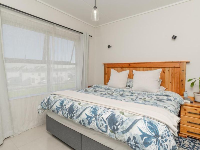 A bright and well-maintained bedroom featuring a large window with natural light, neutral wall finishes, and functional lighting fixtures.