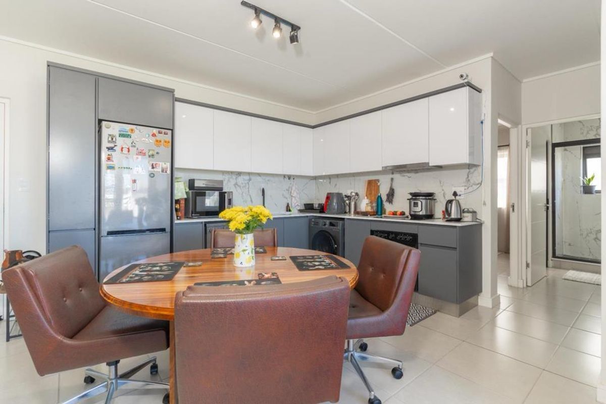Modern kitchen featuring sleek two-tone cabinetry, marble-look backsplash, integrated appliances, and tiled flooring, seamlessly connected to the dining area.