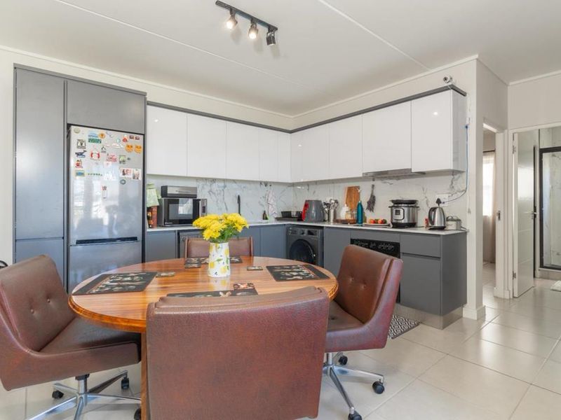 Modern kitchen featuring sleek two-tone cabinetry, marble-look backsplash, integrated appliances, and tiled flooring, seamlessly connected to the dining area.