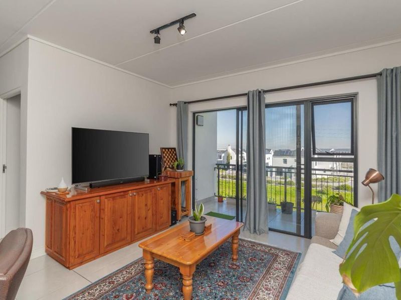 Bright living room featuring tiled flooring, modern track lighting, and large sliding glass doors providing direct access to a private balcony.