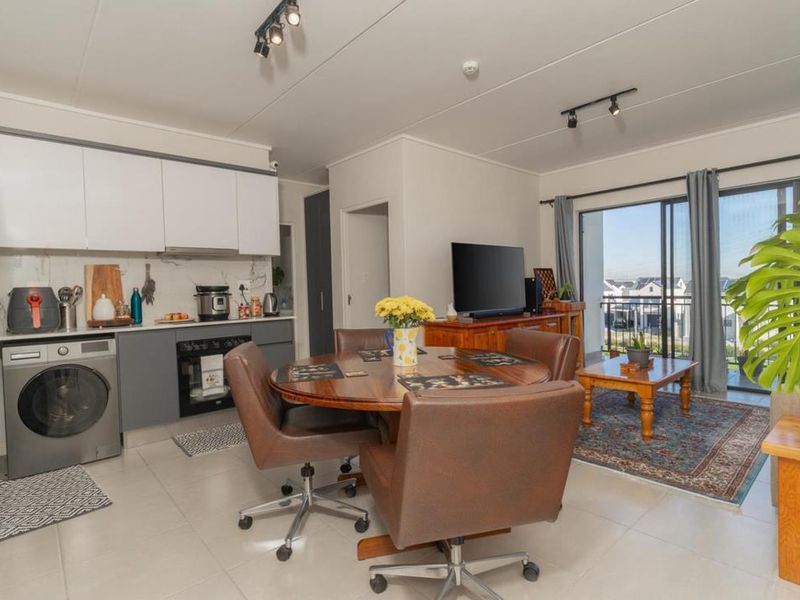 Modern open-plan living area featuring a sleek kitchen with built-in appliances, tiled floors, and large sliding doors leading to a balcony with natural light.