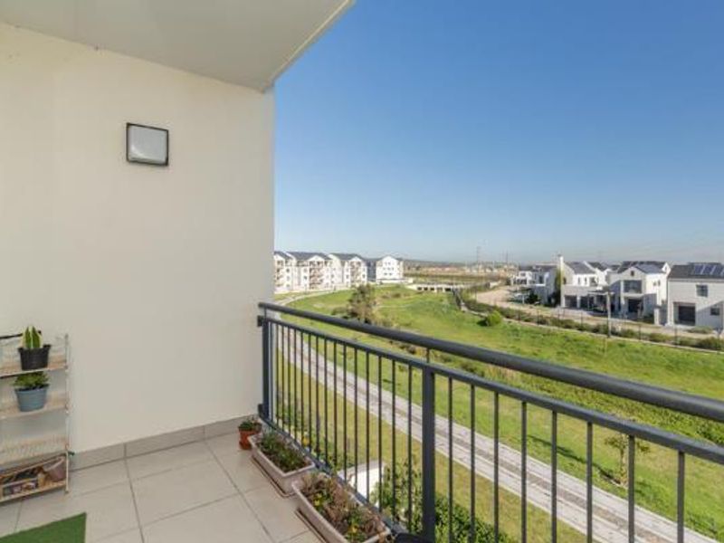 A clean, tiled balcony featuring a metal balustrade and an exterior wall light, offering an open view of the surrounding residential area.