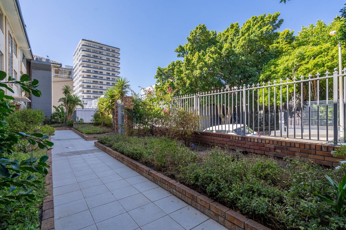 A well-maintained outdoor common area featuring a paved walkway, brick-edged garden beds, and secure metal fencing within an apartment complex setting.