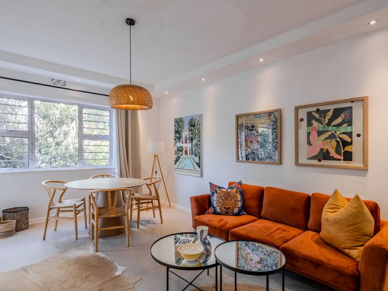 A bright and well-maintained open-plan living and dining area featuring neutral tiled floors, recessed ceiling lighting, and large windows providing natural light.