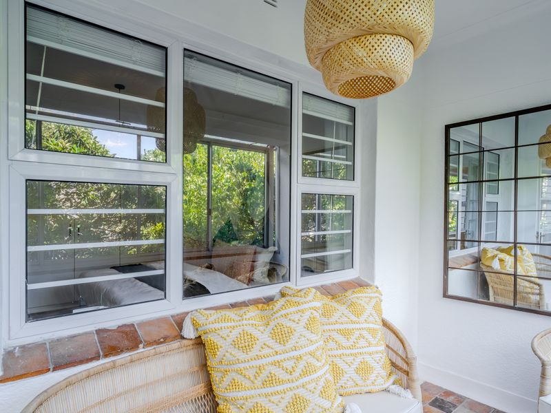 A bright, enclosed patio area featuring terracotta tile flooring, large aluminium-framed windows, and a decorative grid-pattern wall mirror.