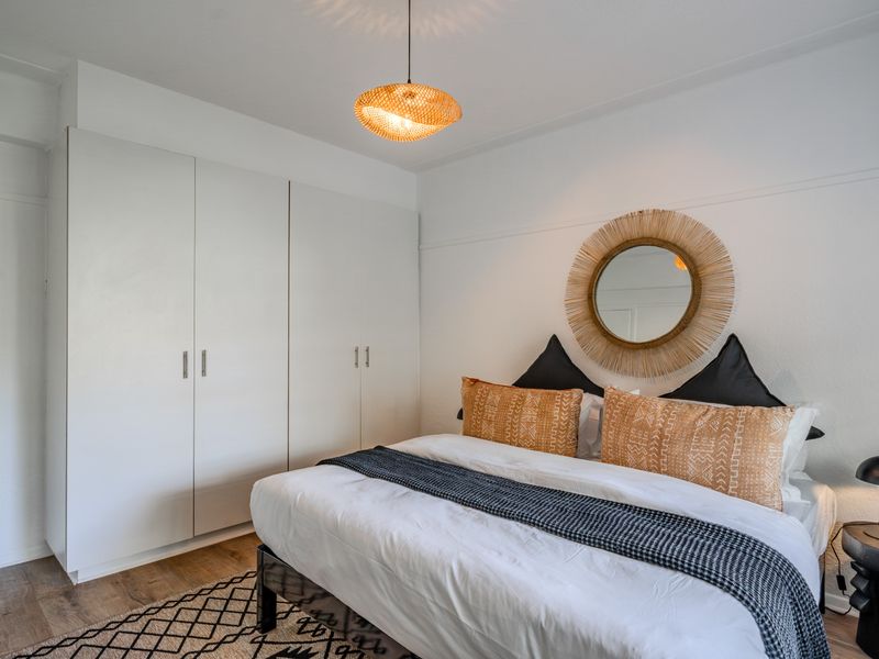 A well-maintained bedroom featuring built-in cupboards, laminate flooring, and a modern pendant light fixture.