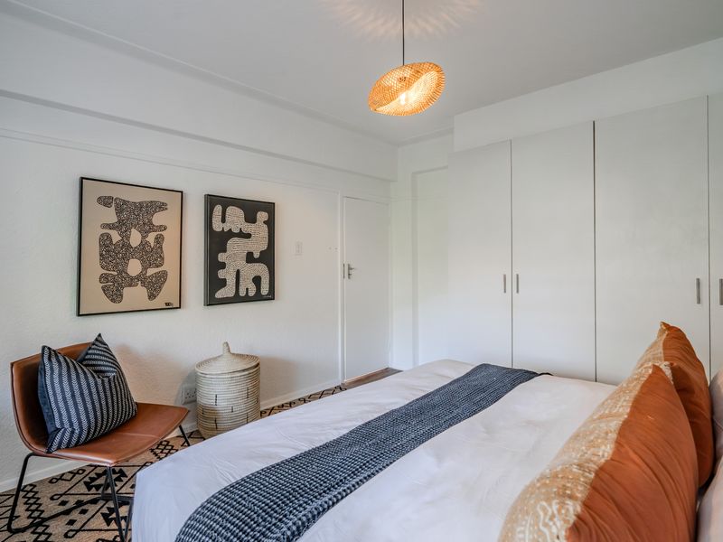 A well-maintained bedroom featuring neutral walls, built-in cupboards, and a modern pendant light fixture.