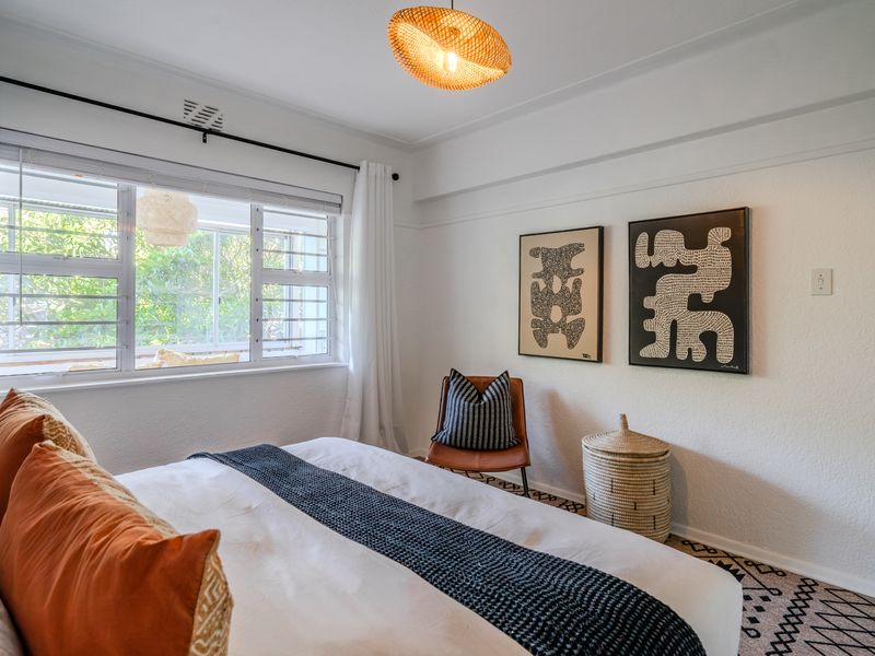 A bright and well-maintained bedroom featuring a large window, classic picture rails, and a modern ceiling light fixture.