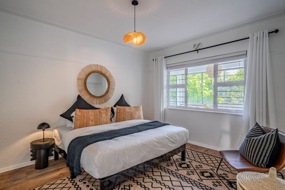 A well-lit bedroom featuring a horizontal sliding window with security bars, classic picture rails, and a modern pendant light fixture.
