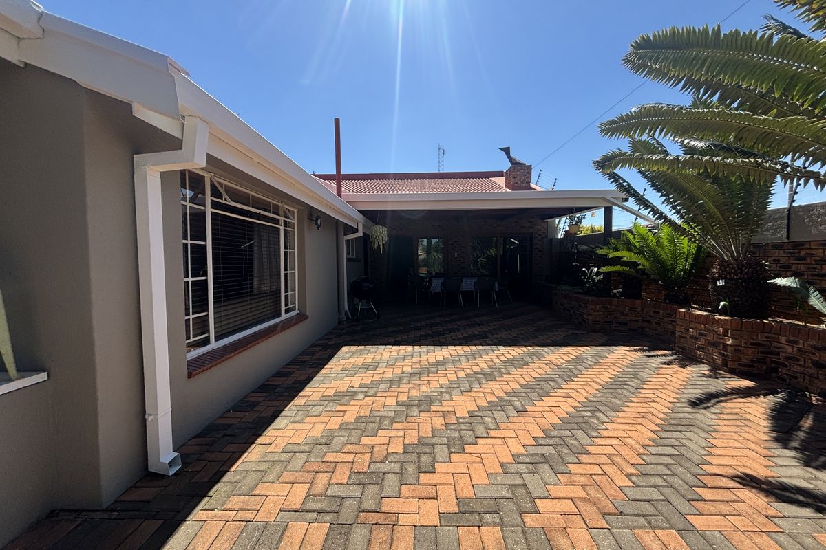 A well-maintained rear exterior featuring a paved patio area, covered outdoor space, and established brick planter boxes under a clear blue sky.