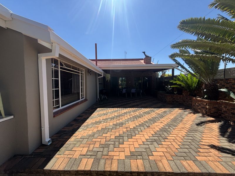 A well-maintained rear exterior featuring a paved patio area, covered outdoor space, and established brick planter boxes under a clear blue sky.