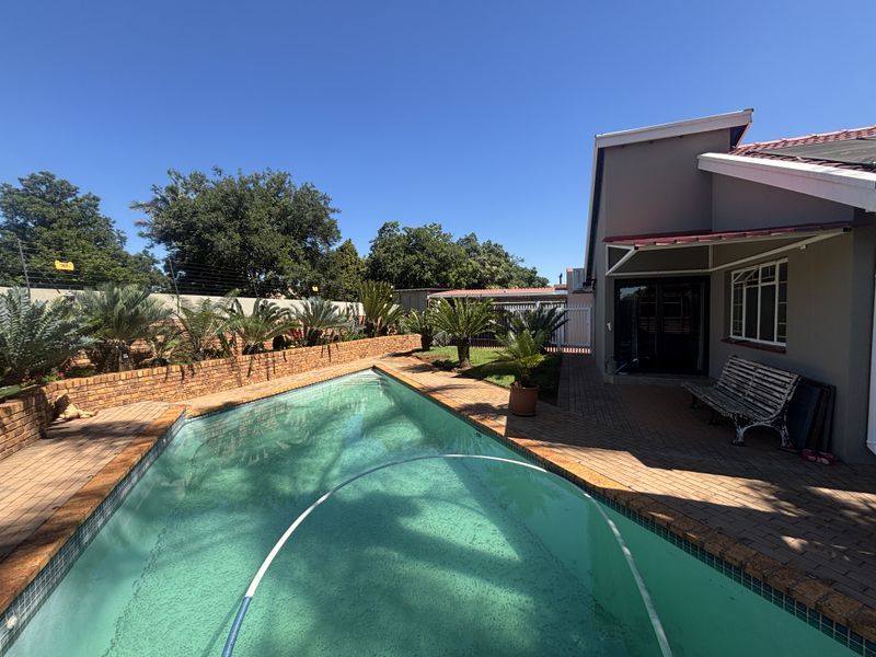 Outdoor pool area featuring a swimming pool, brick paving, and a brick retaining wall, adjacent to the house with a sliding door entrance.