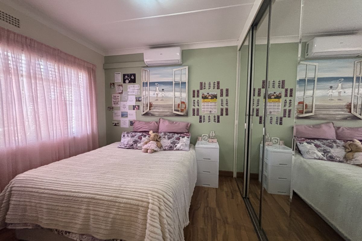 A bedroom featuring laminate flooring, a split-system air conditioner, and a large built-in mirrored wardrobe.