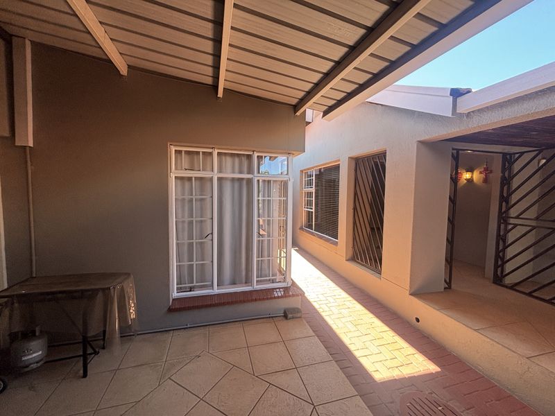 A covered outdoor patio area featuring tiled flooring, brick paving, and secure window frames, providing a functional transition space between the home and garden.