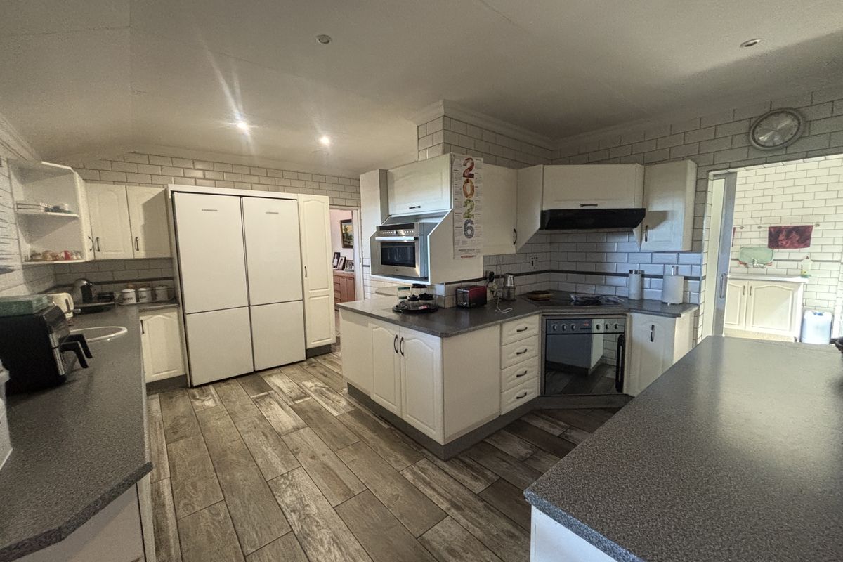 A functional kitchen featuring white cabinetry, subway tile backsplash, integrated appliances, and wood-look flooring, offering a clean and practical workspace.