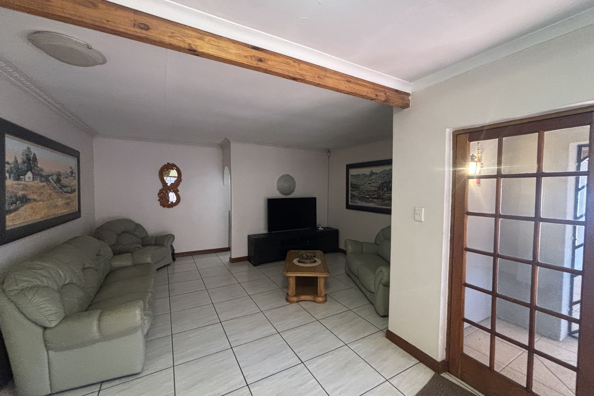 A spacious living room featuring ceramic floor tiles, an exposed timber ceiling beam, and a classic timber-framed glass panel door leading to the exterior.