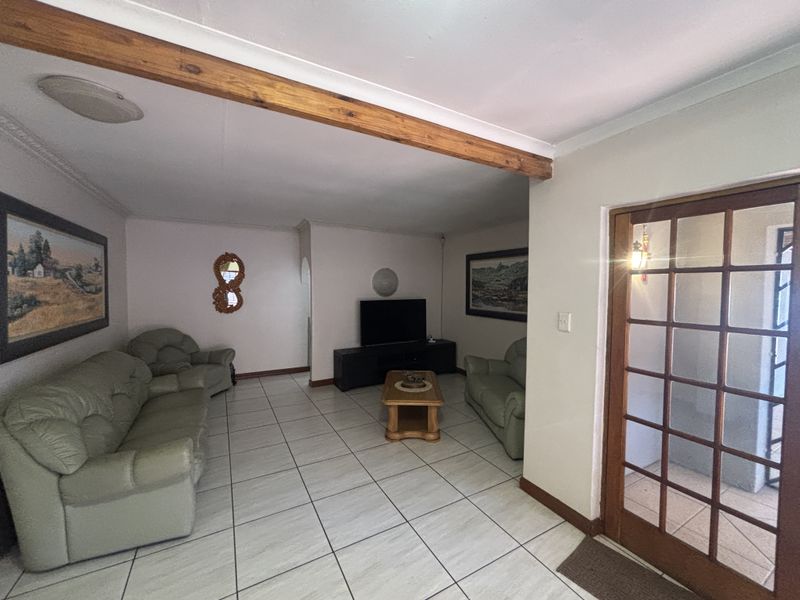 A spacious living room featuring ceramic floor tiles, an exposed timber ceiling beam, and a classic timber-framed glass panel door leading to the exterior.