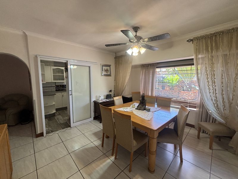 A dining room featuring tiled flooring, a ceiling fan, and a sliding glass door providing access to the kitchen area.