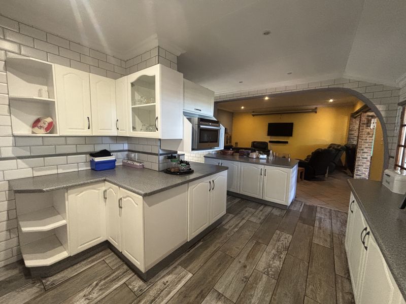 Open plan kitchen featuring white cabinetry, grey laminate countertops, and subway tile backsplash, flowing into an adjacent living area with an arched transition.