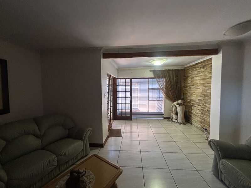 Spacious living area featuring tiled flooring, a decorative stone feature wall, and an exposed timber beam, with direct access to the outdoors via french doors.