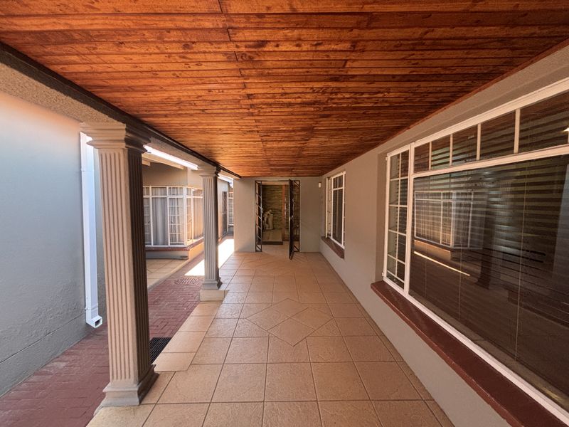A covered patio area featuring a warm wooden ceiling, tiled flooring, and decorative columns, providing a sheltered entrance to the home.