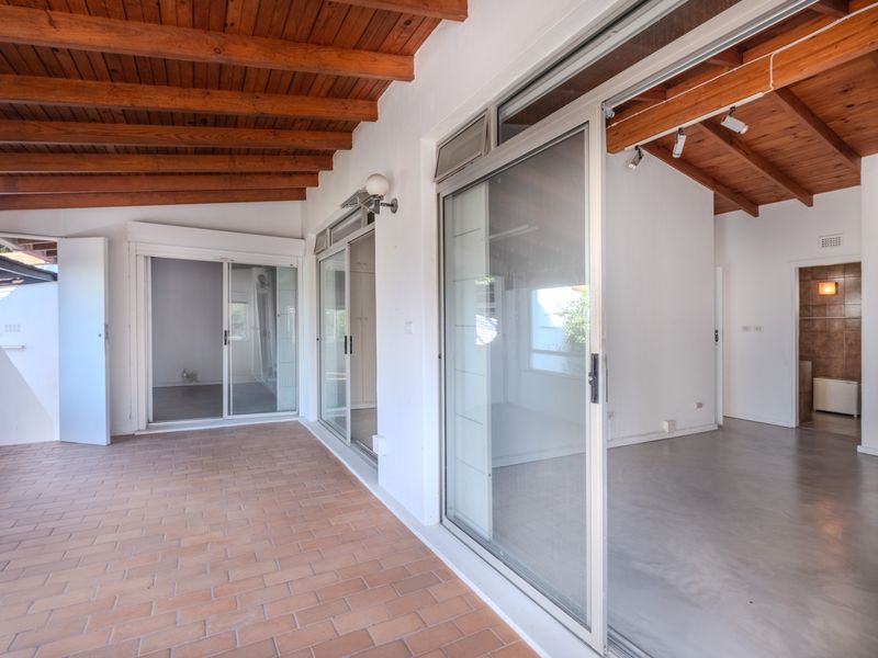 A spacious covered patio featuring exposed timber beam ceilings, terracotta tile flooring, and large aluminium sliding doors providing seamless access to the interior living areas.