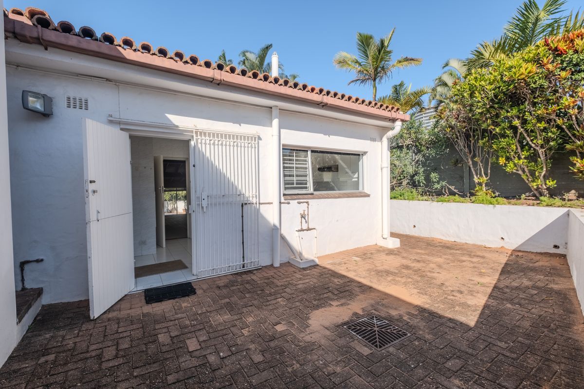 A rear exterior view featuring a paved courtyard, security gate access, and a retaining wall, providing a functional outdoor space.