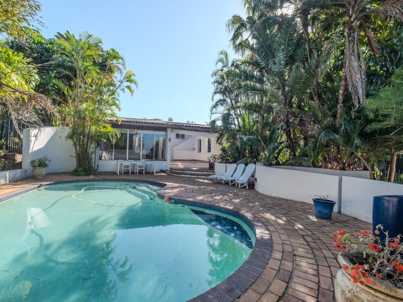 Outdoor pool area featuring a curved swimming pool, brick paved surround, and established tropical landscaping, providing a private space for relaxation and entertainment.