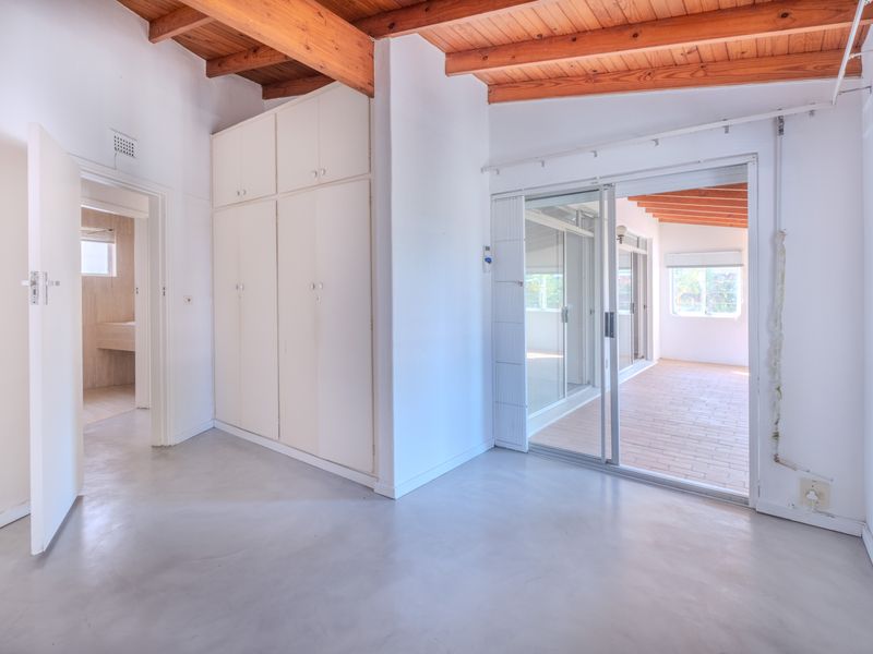 Empty bedroom featuring exposed timber ceiling beams, built-in cupboards, and a sliding glass door leading to an enclosed patio area.