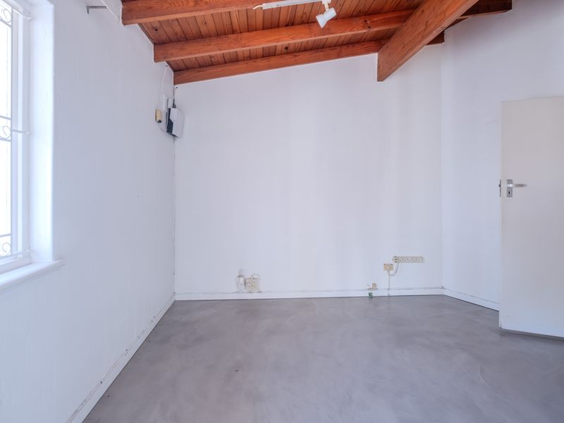 An empty bedroom featuring exposed timber ceiling beams, polished concrete flooring, and a window with a security gate.