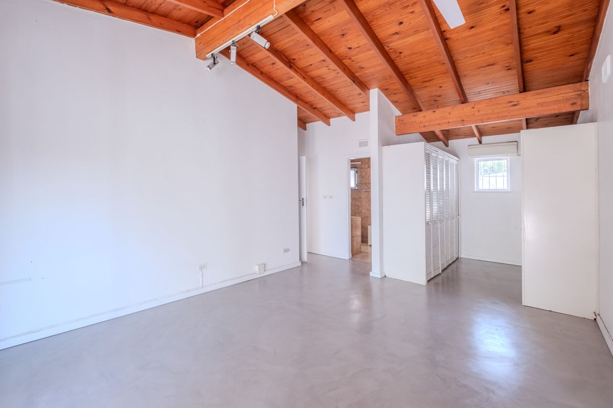 Spacious bedroom featuring exposed timber beam ceilings, polished concrete floors, built-in cupboards, and an en-suite bathroom access.