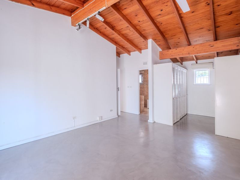 Spacious bedroom featuring exposed timber beam ceilings, polished concrete floors, built-in cupboards, and an en-suite bathroom access.