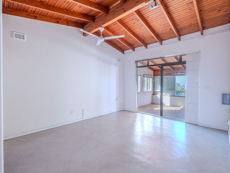 Spacious living area featuring polished concrete floors, exposed timber beam ceilings, and a sliding glass door leading to an outdoor patio.