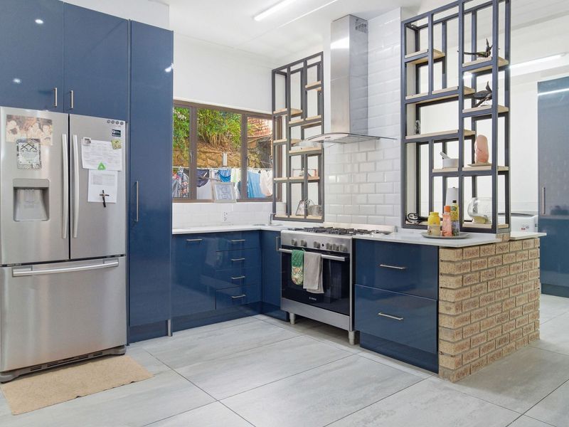 Modern kitchen featuring high-gloss blue cabinetry, subway tile backsplash, gas stove with extractor, and a unique brick-based open shelving partition.