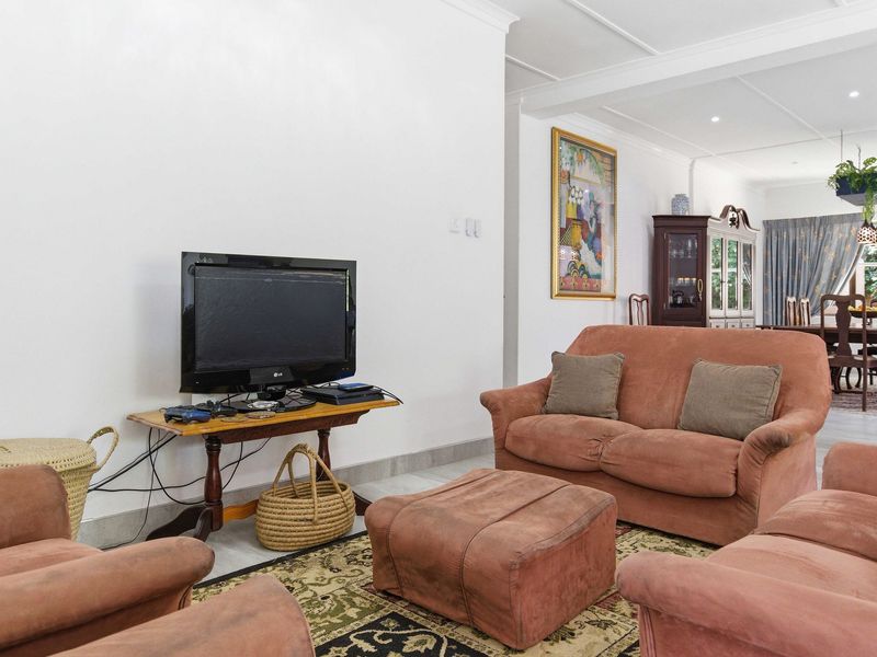A comfortable living room featuring tiled flooring, recessed downlights, and a coved ceiling, flowing into an adjacent dining area.