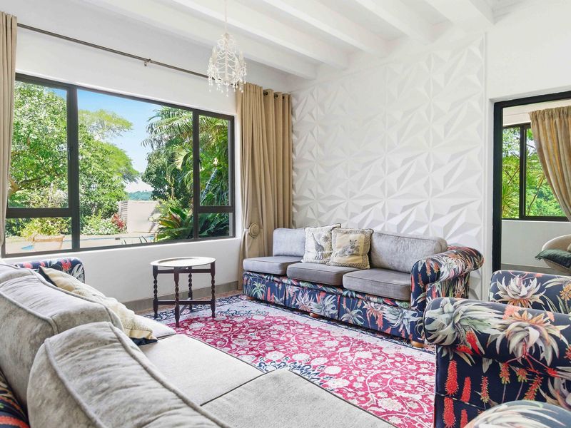 Bright living room featuring exposed ceiling beams, a modern textured feature wall, and large windows providing natural light and garden views.