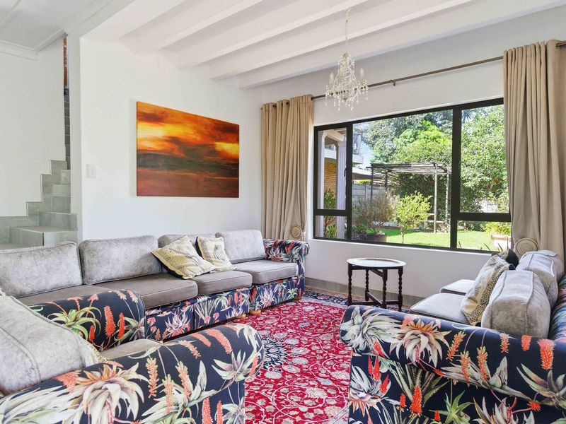 A bright living room featuring exposed beam ceilings, a large window overlooking the garden, and an adjacent staircase.