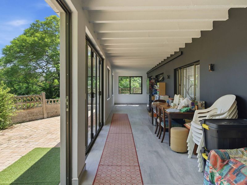 A covered patio area featuring exposed beam ceilings, tiled flooring, and large sliding glass doors that provide seamless access to the outdoor garden space.