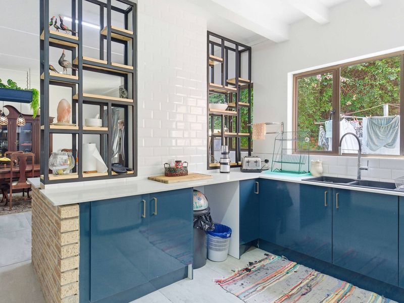 Modern kitchen featuring blue cabinetry, quartz countertops, subway tile backsplash, and unique custom metal shelving units with an exposed brick base.