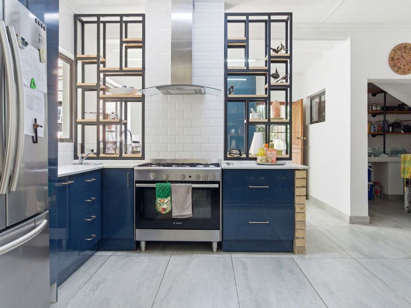 Modern kitchen featuring navy blue cabinetry, subway tile backsplash, stainless steel gas stove with extractor fan, and open decorative shelving.